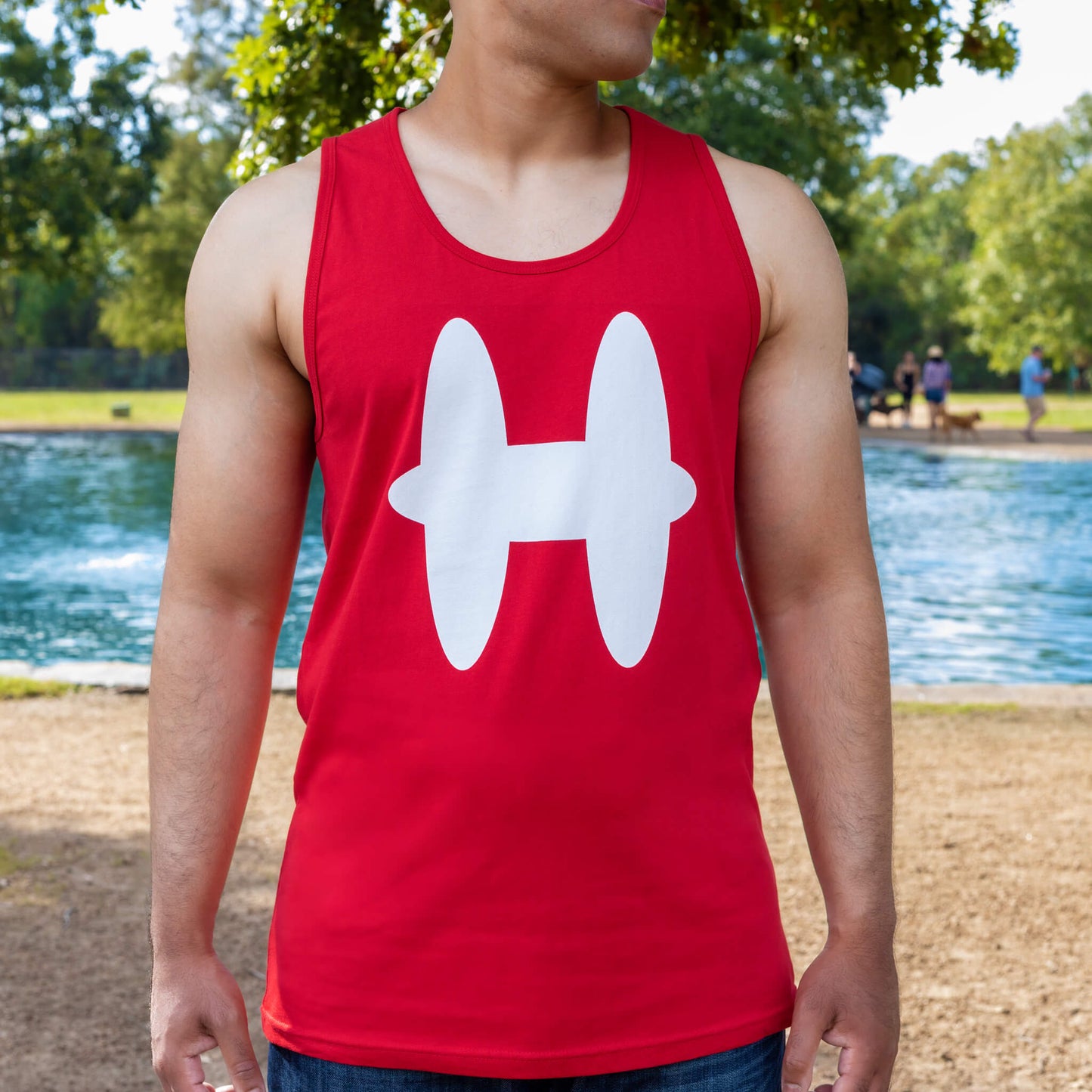Man wearing red Houmane tank top with white H logo. Dog park in background.