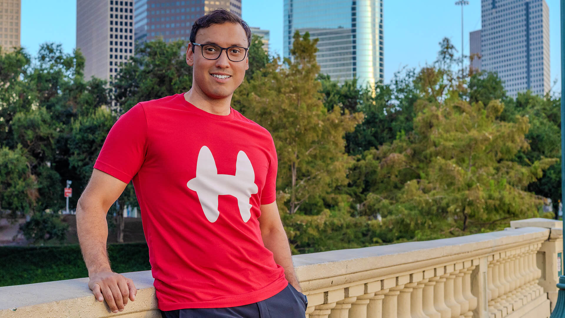 Man wearing red Houmane t-shirt with white H logo. Houston skyline in the background. 